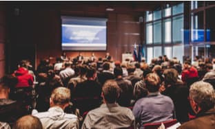 a crowd listening to a panel at a business conference 